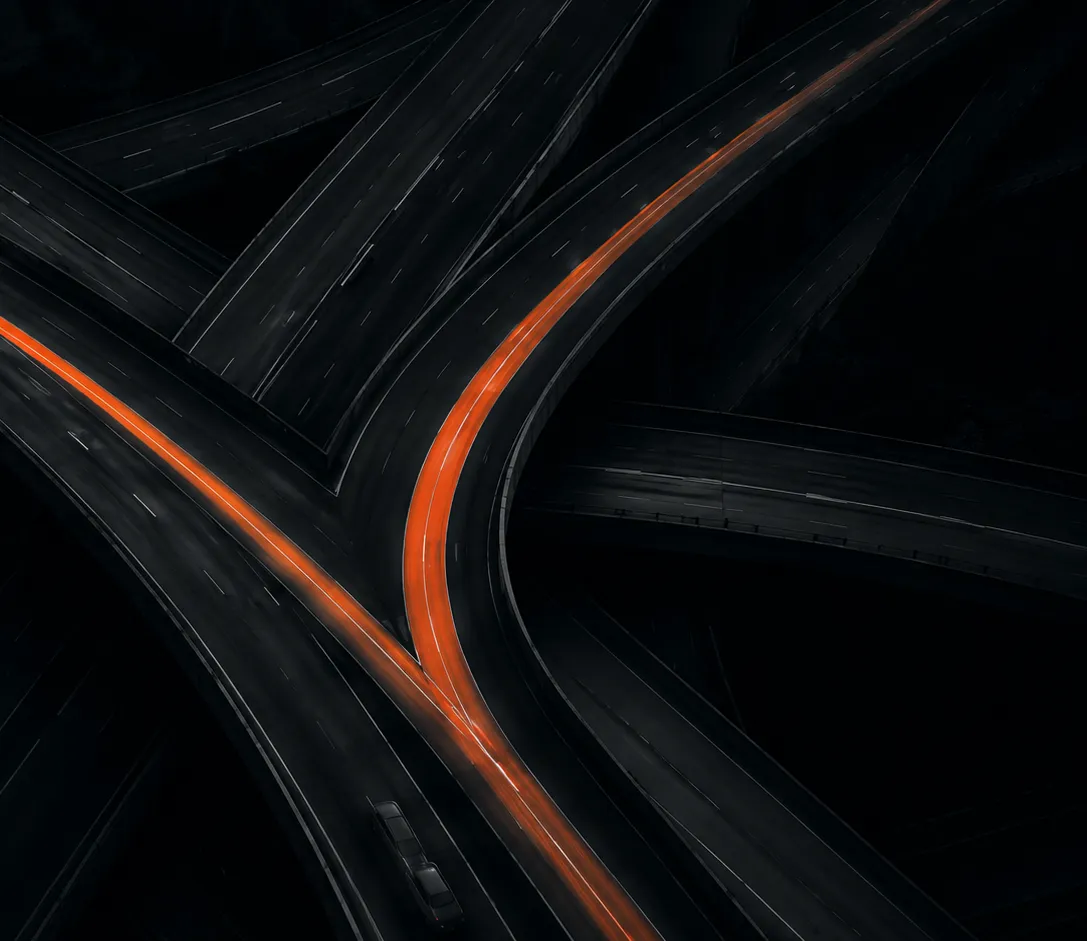 Entroncamento de rodovias visto de cima, com uma faixa iluminada em laranja se destacando entre as demais pistas